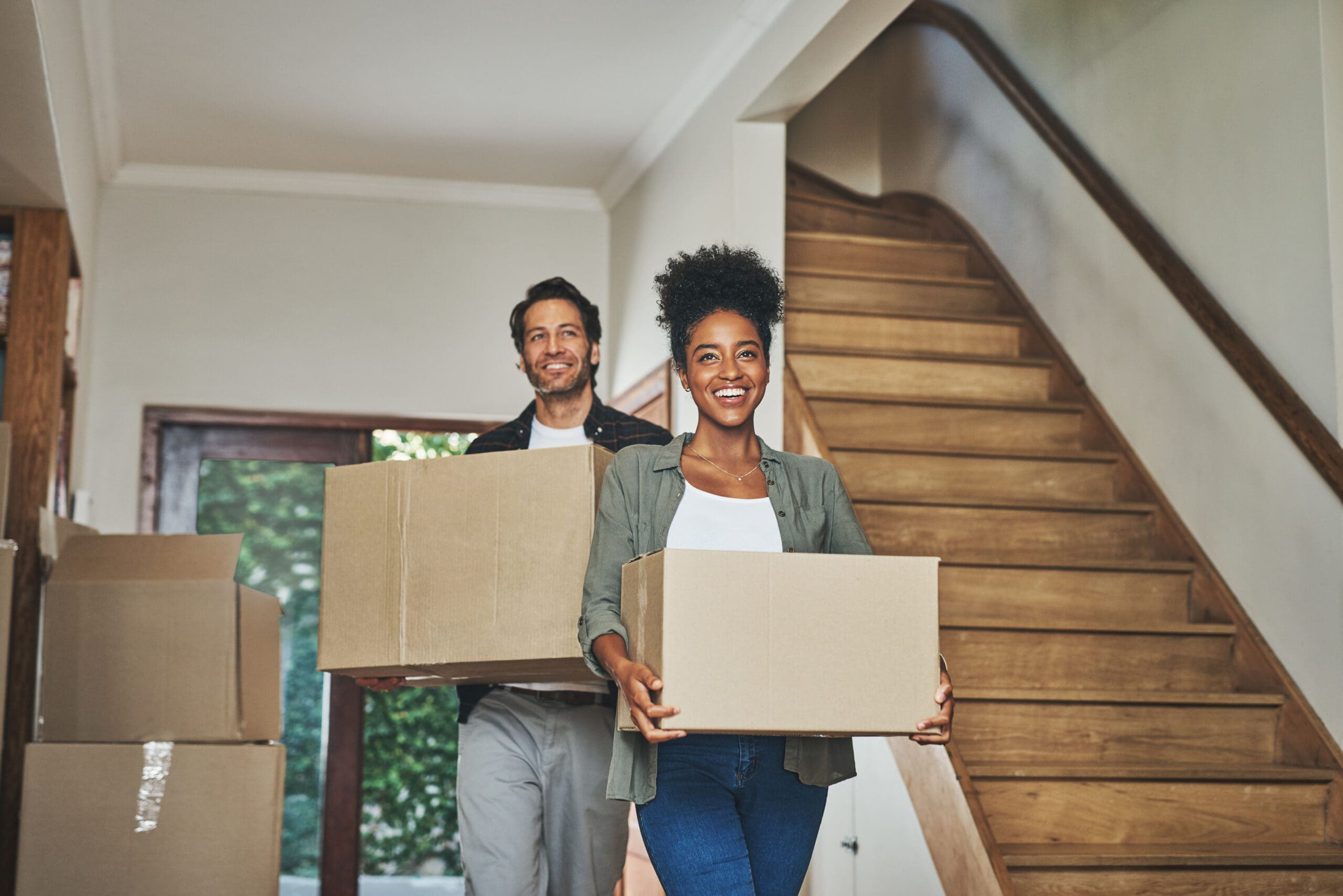 Happy couple, real estate and moving in new home with boxes for renovation, investment or relocation. Interracial man and woman owner carrying box for property rent, mortgage loan or move together.