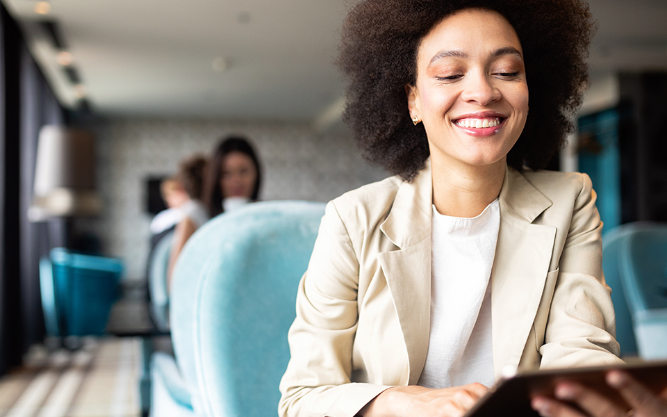 MM-Acct-960x600 – Capital Bank A woman in business clothing is seated in a resaurant. She appears to be looking at the screen of a tablet