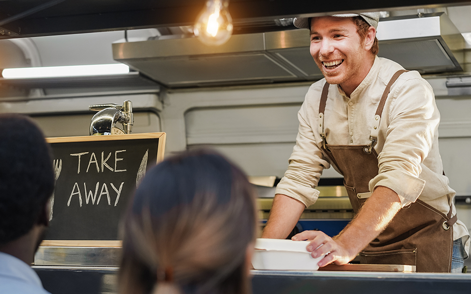 A man working in a food truck hands food to a customer