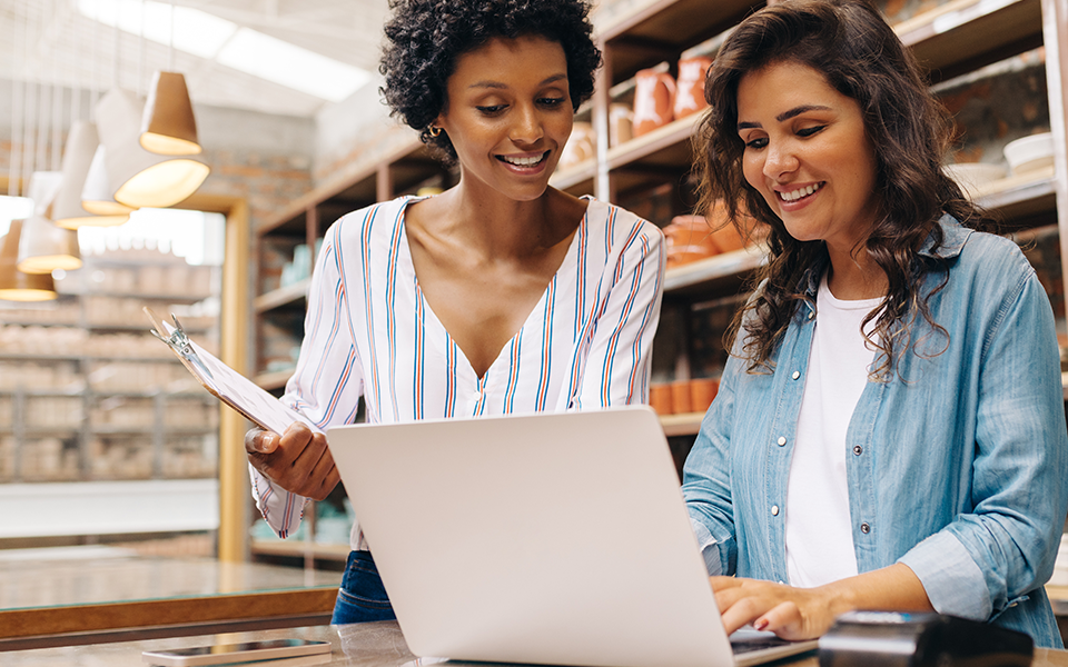 Positive-Pay-960x600 – Capital Bank A woman works on a laptop while her colleague stands near by holding a clipboard looking at the screen