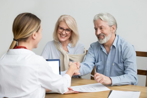 Photo of a man and woman sitting at the table, meeting with a woman who has her back to the camera as she faces the couple