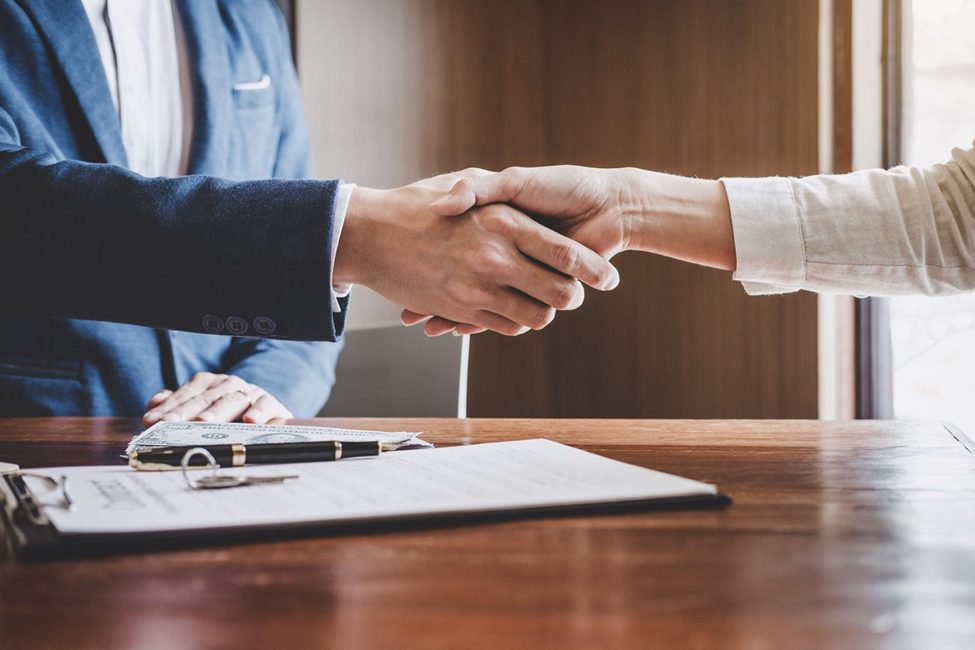 Closeup image of a man and woman shaking hands over a signed business agreement