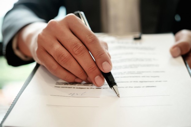 close up photo of hand holding a pen as the person appears to be reviewing a contract