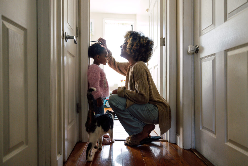 An African American woman squatting down to measure her daughter against the door frame.
