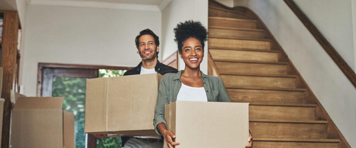 Happy couple, real estate and moving in new home with boxes for renovation, investment or relocation. Interracial man and woman owner carrying box for property rent, mortgage loan or move together.