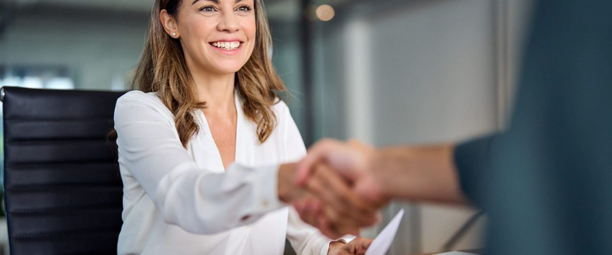 Happy mid aged business woman manager handshaking at office meeting. Smiling female hr hiring recruit at job interview, bank or insurance agent, lawyer making contract deal with client at work.