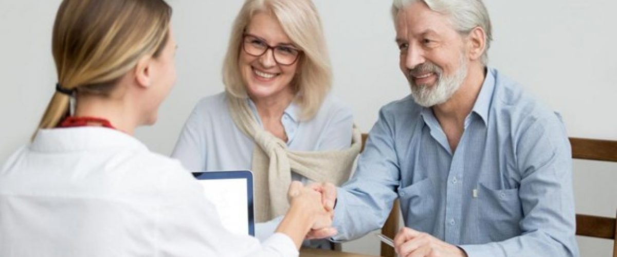 Photo of a man and woman sitting at the table, meeting with a woman who has her back to the camera as she faces the couple