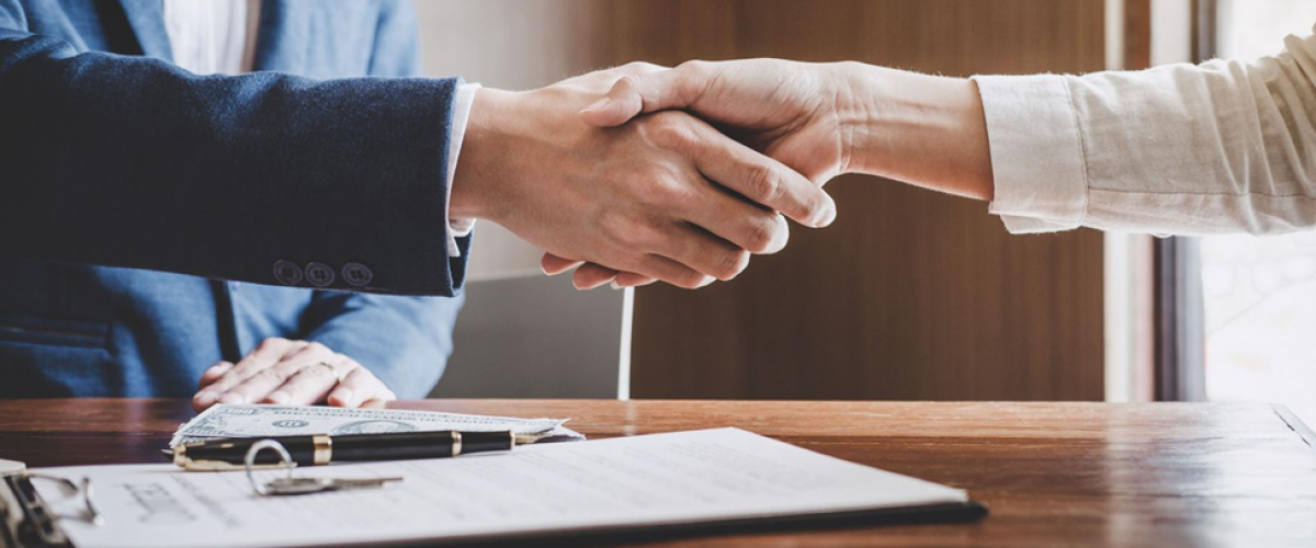 Closeup image of a man and woman shaking hands over a signed business agreement