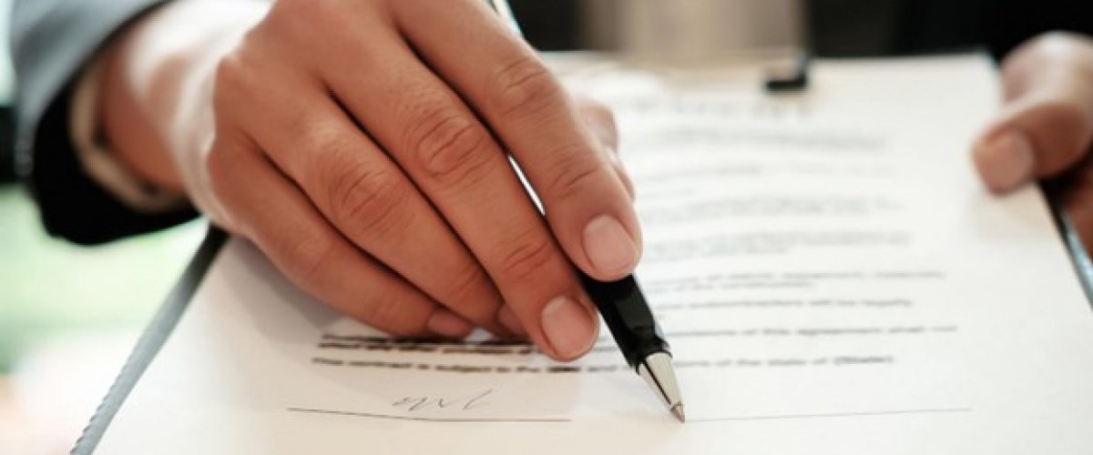 close up photo of hand holding a pen as the person appears to be reviewing a contract