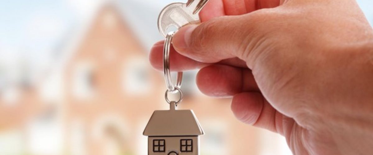 Close up photo of a hand holding a key with a small model of a house as a key chain